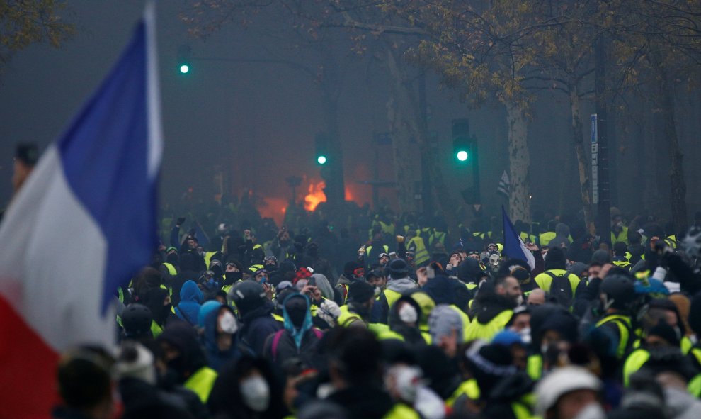 Entre el fuego y la bandera de Francia, cientos de manifestantes de los chalecos amarillos que protestan contra la subida de impuestos a los carburantes.- Stephane Mahe/REUTERS