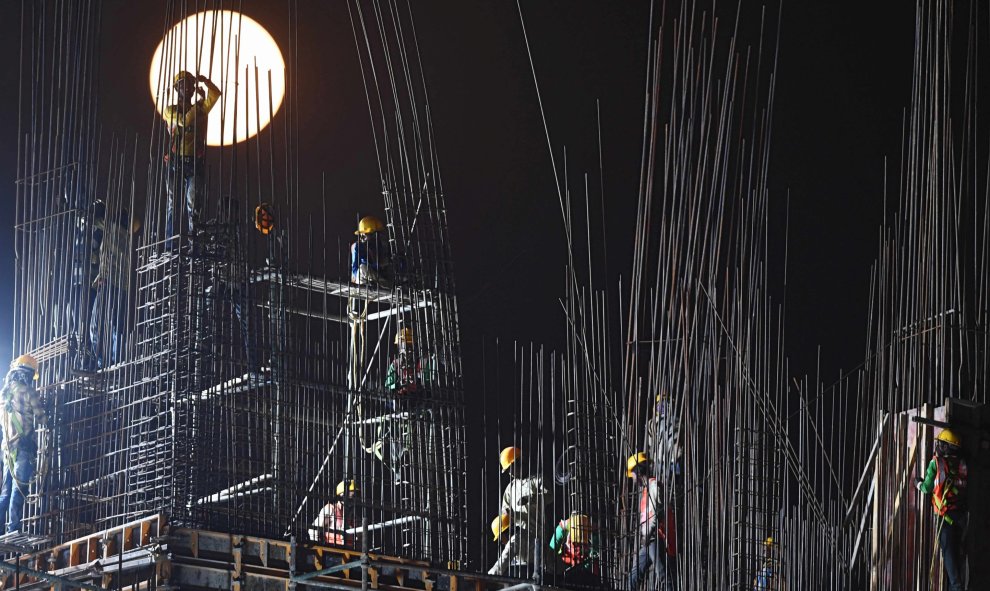 La luna de nieve se eleva cuando unos obreros de la construcción trabajan en una obra en Kolkata, Calcuta, India | AFP/ Dibyangshu Sarkar