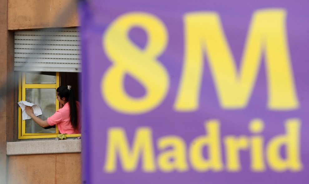 Una mujer limpia una ventana junto a un cartel alusivo al Día Internacional de la Mujer, este viernes en Madrid. EFE/Chema Moya