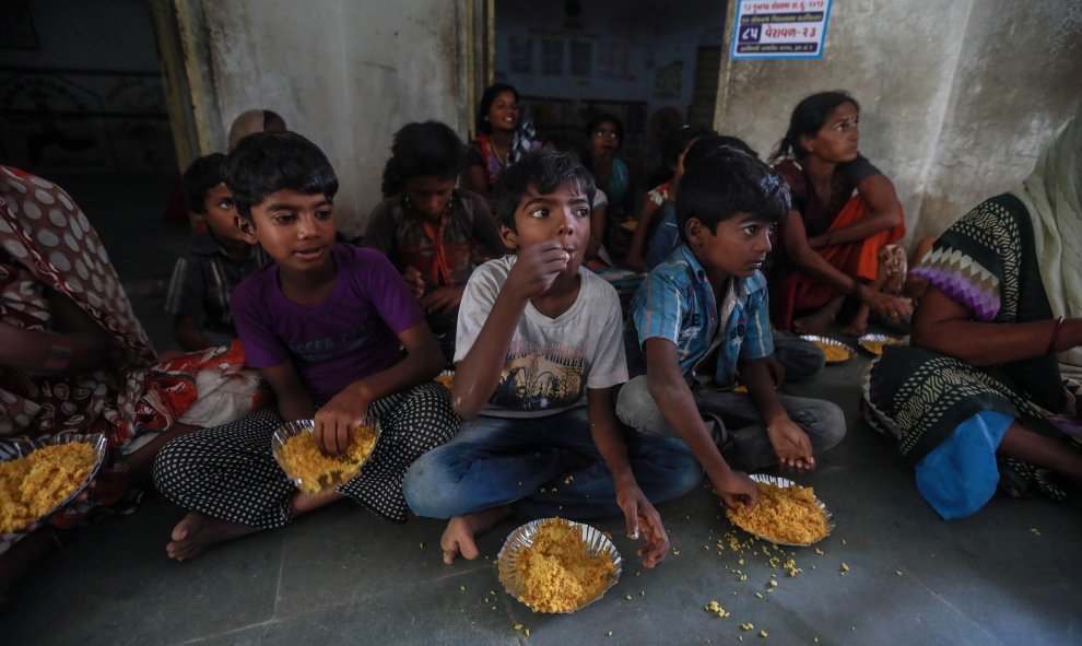 Un grupo de niños de uno de los refugios habilitados se disponen a comer los alimentos distribuidos por una ONG tras el paso del 'ciclón Vayu' este jueves en Veraval (India). | EFE