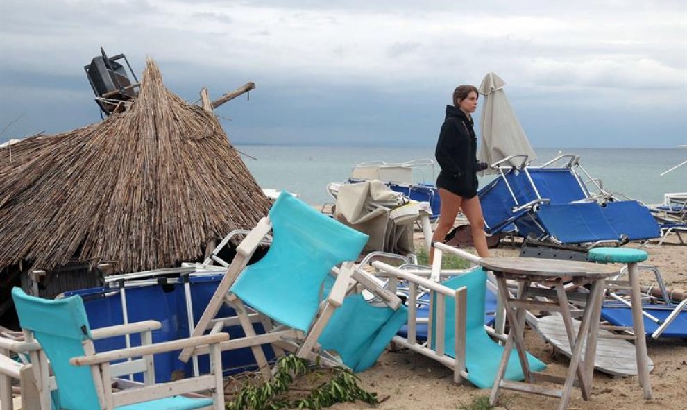 Una mujer camina entre sillas volcadas por el temporal en Grecia. EFE/EPA/VERVERIDIS VASSILIS