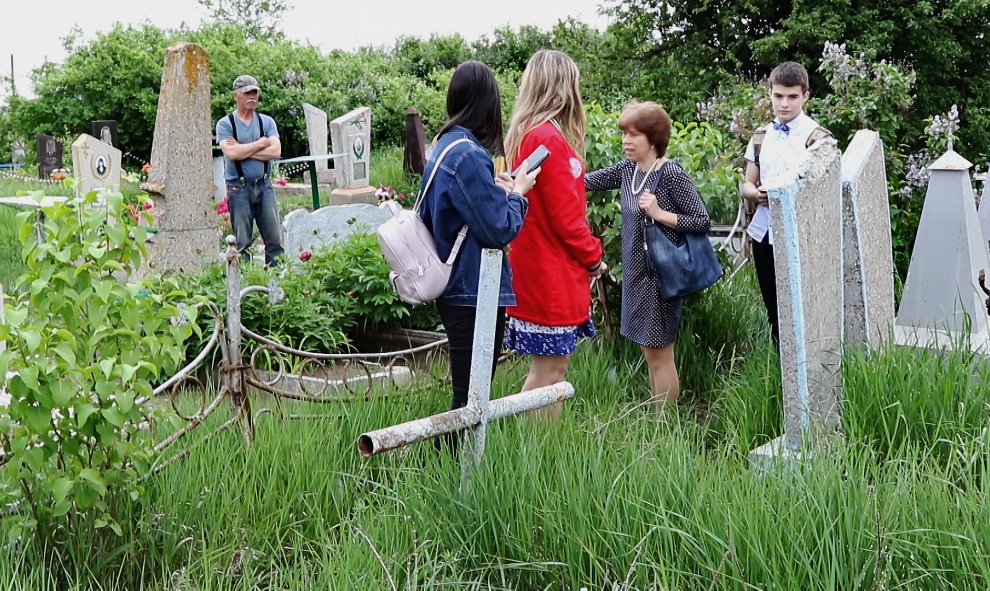 Yuri Ivanovich visita la tumba de los padres y hermanos de Néstor, entre ellos, su bisabuelo, en el cementerio de Guliai Pole, junto a una profesora y varios alumnos de un centro educativo. / Ferrán Barber