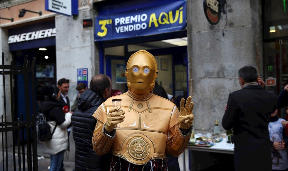 Una persona disfrazada del androide de la Guerra de las Galaxias C-3PO celebra en la administración de lotería 150 en la calle Arenal de Madrid. EFE/Rodrigo Jiménez