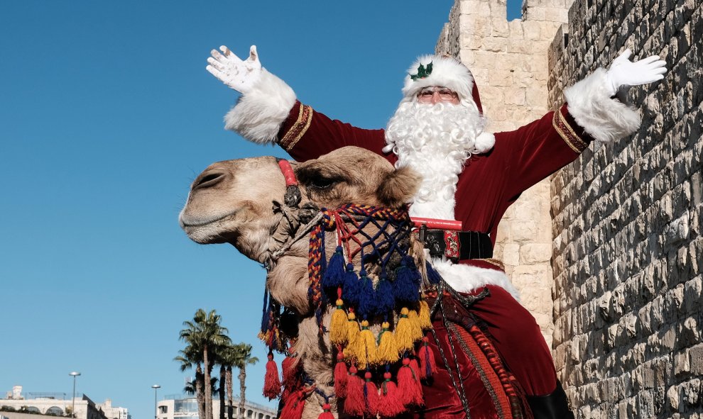 Un hombre customizado de Santa Claus monta en camello en Jerusalén. EUROPA PRESS