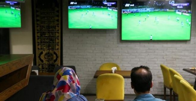 Una mujer ve un partido de fútbol junto a un amigo en una cafetería de Irán. REUTERS