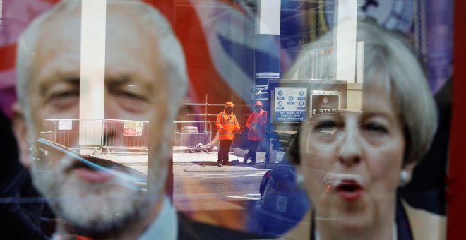 Trabajadores instalando vallas de seguridad se reflejan en el escaparate de una tienda con imágenes de la Primera Ministra británica Theresa May y el candidato laborista Jeremy Corbyn en Londres. REUTERS/Marko Djuric