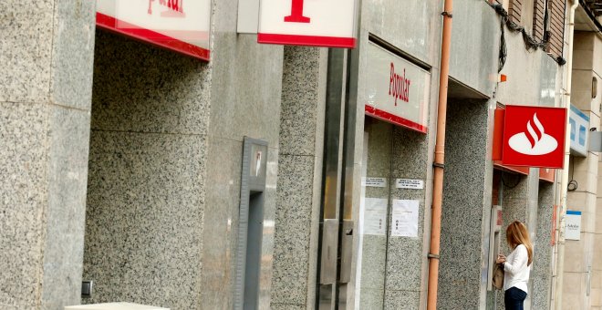 Una mujer usa un cajero automático en una oficina del Banco Santander junto a una sucursal del Banco Popular. REUTERS/Albert Gea