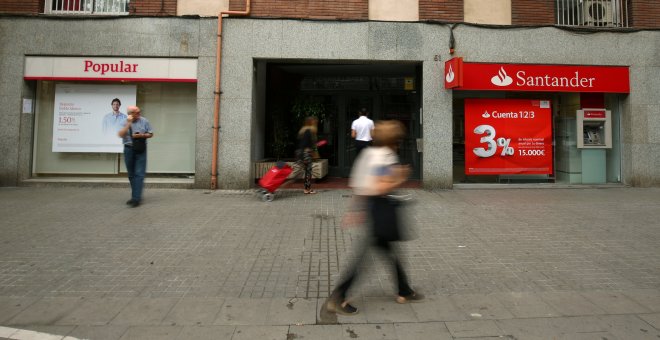 Varios personas pasan junto a sendas oficinas de Banco Popular y Banco Santander, en Barcelona. REUTERS/Albert Gea