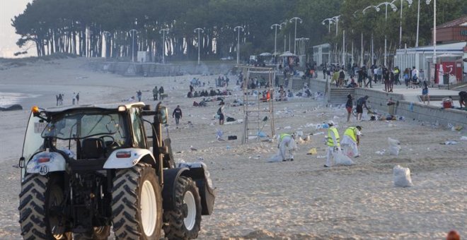 Varios operarios limpian la playa del Samil, en Vigo, tras la jornada festiva de las Hogueras de San Juan. EFE/Salvador Sas