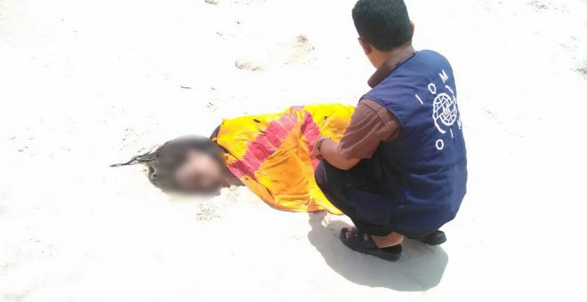 un trabajador de la Organización Internacional para las Migraciones (OIM) junto al cadaver semienterrado de uno de los  jóvenes migrantes fallecidos frente a las costas de Yemen. EFE