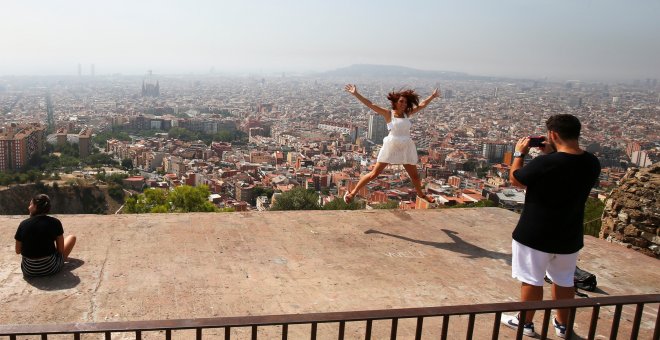 Una joven turista salta,mientras le toman una foto con el 'skyline' de Barcelona a su fondo. REUTERS/Albert Gea