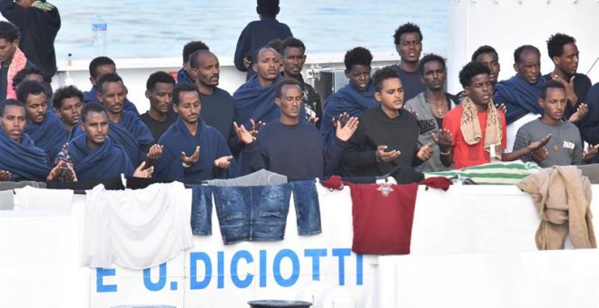 Migrantes rezan a la espera del desembarco del barco italiano de la Guardia Costera italiana en Catania. - EFE