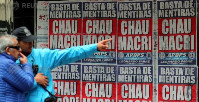 Un agente de Policía da indicaciones a un hombre en el distrito financiero de Buenos Aires junto a un cartel contra Mauricio Macri, el presidente de Argentina. - REUTERS
