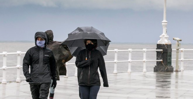 Un grupo de personas paseando por la playa de San Lorenzo de Gijon, bajo un fuerte chubasco y viento - EFE/Alberto Morante