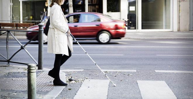 Una persona con discapacidad visual cruzando un paso de peatones ayudándose con un bastón. / ONCE