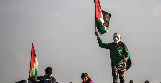 21/12/2018.- Un protestante palestino ondea una bandera nacional durante los enfrentamientos cerca de la frontera entre Israel y la Franja de Gaza, hoy, 21 de diciembre de 2018. Un menor palestino murió y doce resultaron heridos hoy por disparos del Ejérc