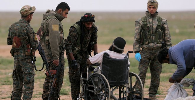 Combatientes de las Fuerzas Democráticas Sirias junto a un hombre en silla de ruedas en la ciudad de Baghouz. /REUTERS