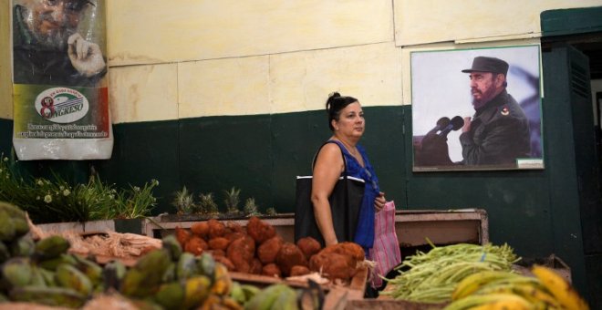 Una mujer compra verduras junto al póster del difunto líder cubano Fidel Castro en un mercado en La Habana. AFP/Yamil Page