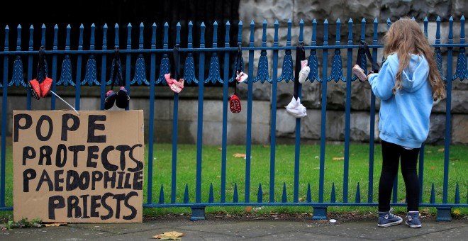 Una niña cuelga un zapato de bebé en una valla para protestar contra los abusos de la Iglesia. - REUTERS