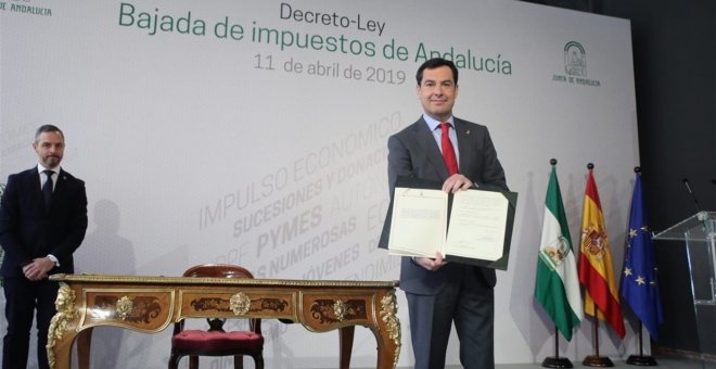 El presidente Juanma Moreno muestra el decreto-ley de rebaja fiscal que acaba de firmar junto a su consejero de Hacienda, Juan Bravo.