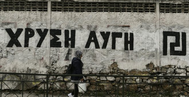 Una mujer pasa junto a una pared pintada con el logotipo del partido neonazi griego Amanecer Dorado, en Atenas. AFP/Aris Messinis