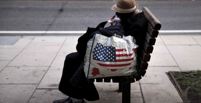 Una mujer sin hogar descansa en un banco.- AFP