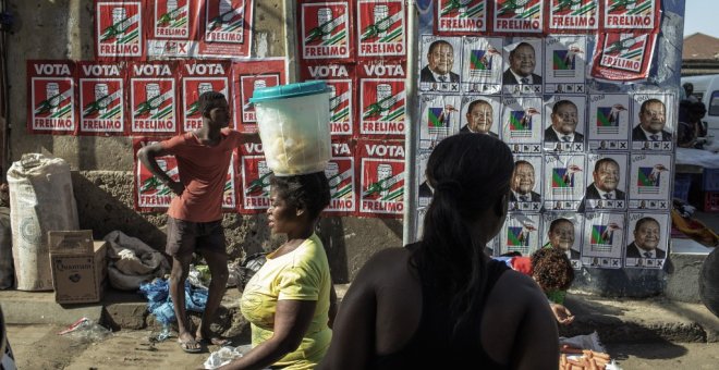 Vendedores y clientes caminan por un muro cubierto con carteles de la campaña de las elecciones presidenciales de Mozambique en el mercado Xipamanine en Maputo. - AFP