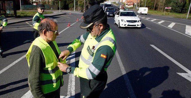 Un guardia civil coloca un chaleco reflectante a un peatón. / EFE