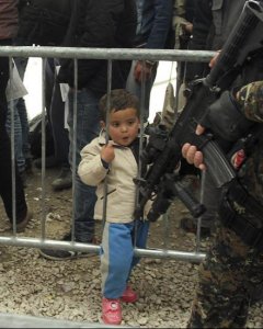 Un niño refugiado contempla el arma de un militar serbio, mientras espera para ser registrados en el campo de refugiados de Presevo, al sur de Serbia. EFE/Djordje Savic