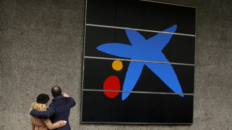 Una pareja se hace un selfi junto al logo de Caixabank en su sede en Madrid. REUTERS/Sergio Perez