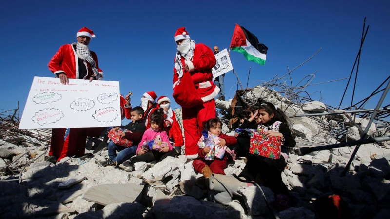 Jóvenes vestidos de Papa Noel junto a varios niños en los escombros de una casa palestina demolida por fuerzas israelíes en Bethlehem, Cisjordania. - REUTERS