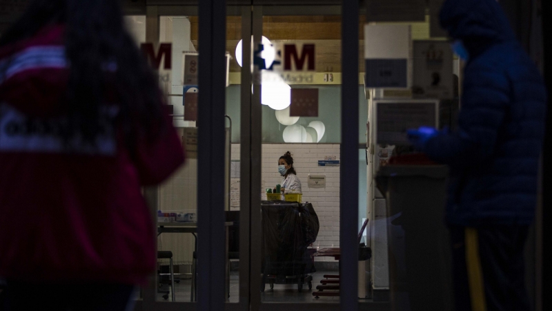 Las puertas de un hospital madrileño muestran personas esperando con mascarillas y guantes y una trabajadora sanitaria. / JAIRO VARGAS