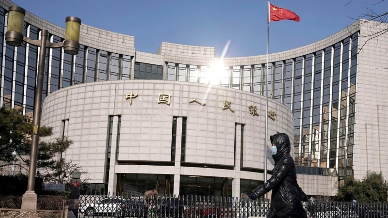 Una mujer con mascarilla pasa por delante de la sede del Banco Popular de China, el banco central del país asiático, en Pekín. REUTERS/Jason Lee