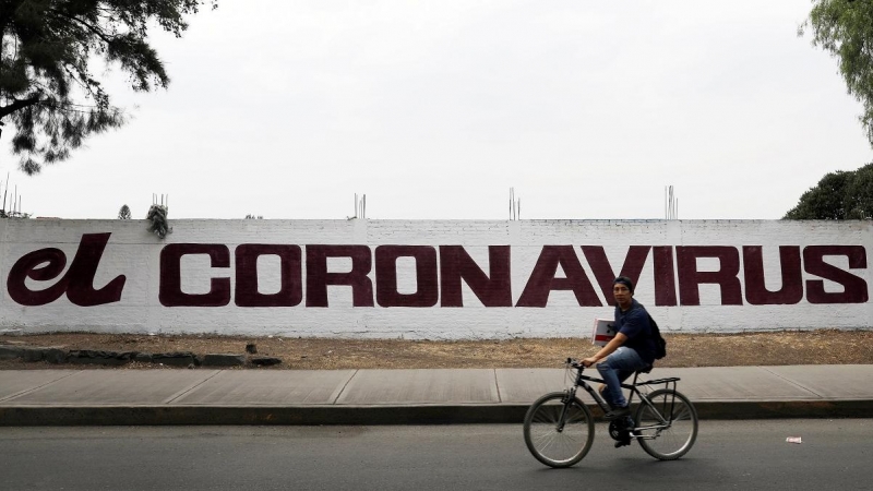 Un ciudadano pedalea con su bicicleta junto a un muro con una pintada que hace referencia al coronavirus. REUTERS/Carlos Jasso