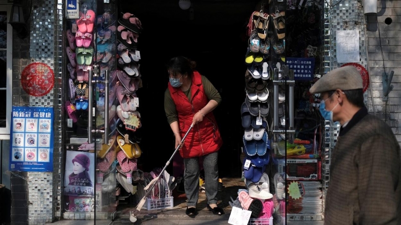 Una mujer con mascarilla limpia la entrada de su tienda en Pekín.. REUTERS/Carlos Garcia Rawlins
