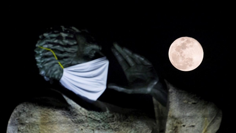 Fotografía de la luna llena denominada la superluna de las flores junto a la estatua de fray Antonio de Montesino este jueves en Santo Domingo (República Dominicana). La estatua de 15 metros de altura tiene una mascarilla como alerta sobre el coronavirus.