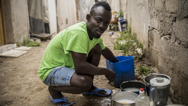 Sai, de 19 años, y procedentes de Ghana, friega los utensilios de cocina junto a la chabola en la ha vivido los tres años, desde que cruzó el Estrecho en patera. Durante más de un mes ha sido incapaz de encontrar trabajo debido a las restricciones del est