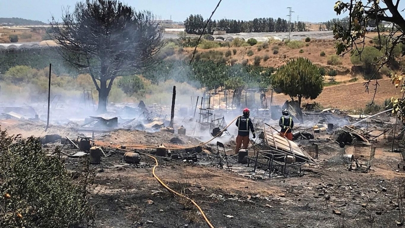 Miembros de los servicios de bomberos extinguen las llamas tras un incendio declarado en un asentamiento chabolista de Lepe, Huelva. - EFE