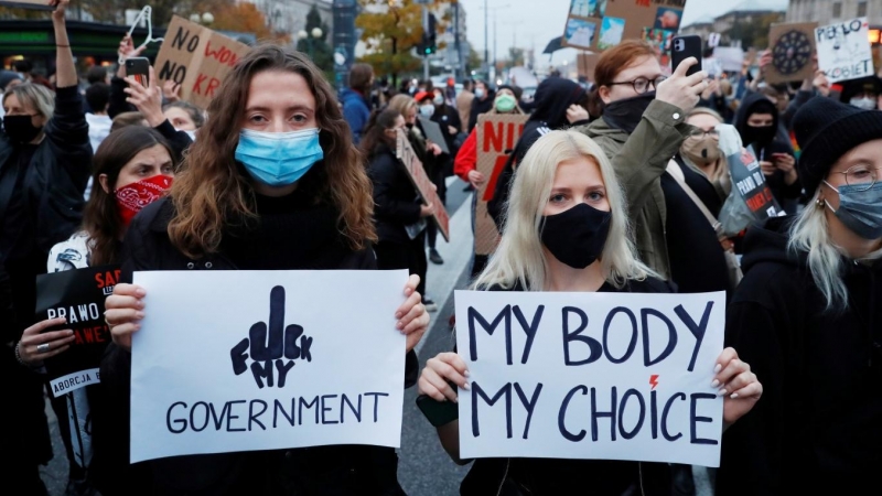 A la izquierda, una manifestante sostiene un cartel en contra del gobierno polaco ('Fuck my Government'), a la derecha, otra joven lleva un cartel que reza 'My body, my choice' ('Mi cuerpo, mi elección').