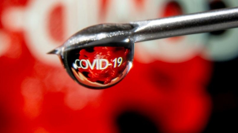 La palabra 'covid-19' se ve reflejada en la gota de una jeringuilla.