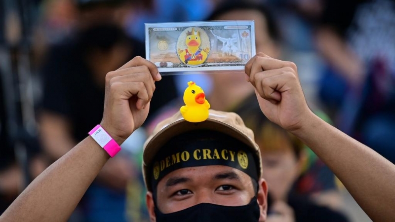 Un manifestante a favor de la democracia con un pequeño pato de goma en su gorra sostiene un billete simulado durante una manifestación contra el gobierno frente a la sede del Siam Commercial Bank en Bangkok.