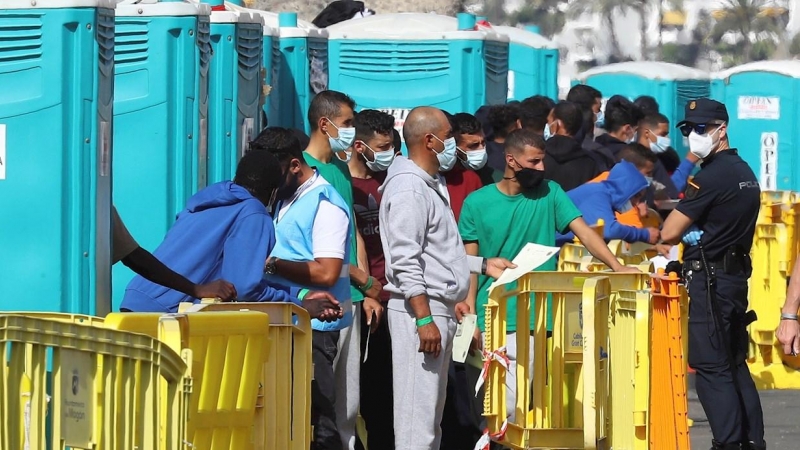 Varios migrantes esperan en el muelle de Arguineguín (Gran Canaria) a que les tomen las huellas dactilares y la filiación.