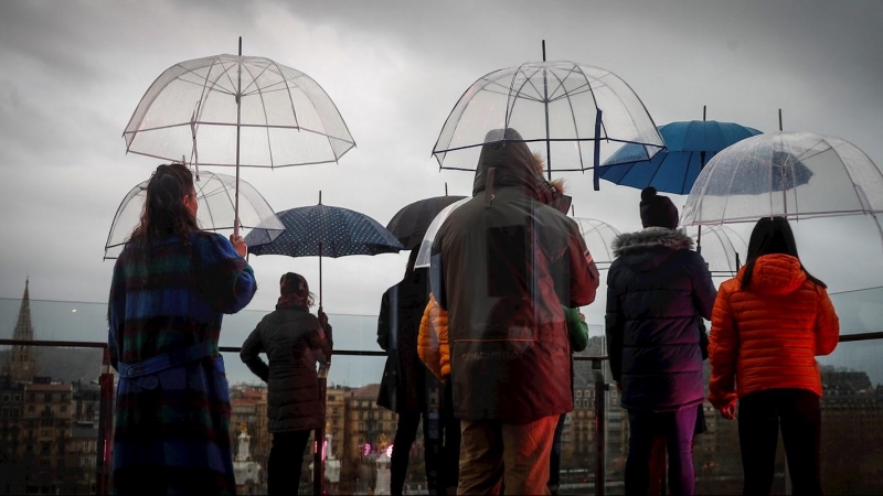 Varias personas se protegen de la lluvia con sus paraguas este miércoles en la terraza del centro cultural Tabakalera de San Sebastián