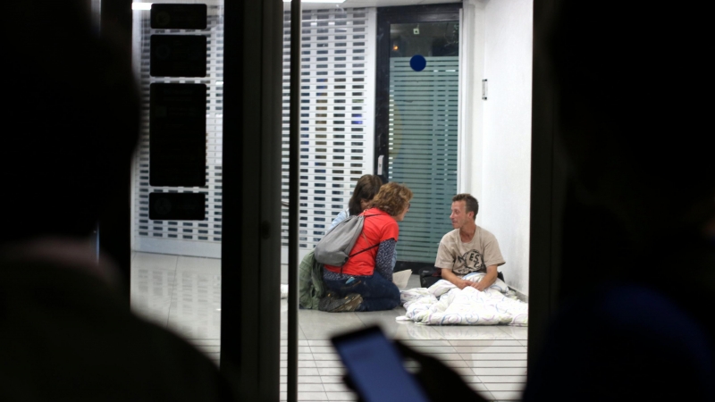 Dins un caixer la Berta i la Clara conversen amb un home mentre la resta de voluntaris del grup els espera a fora durant el cens de persones sense llar de Barcelona.
