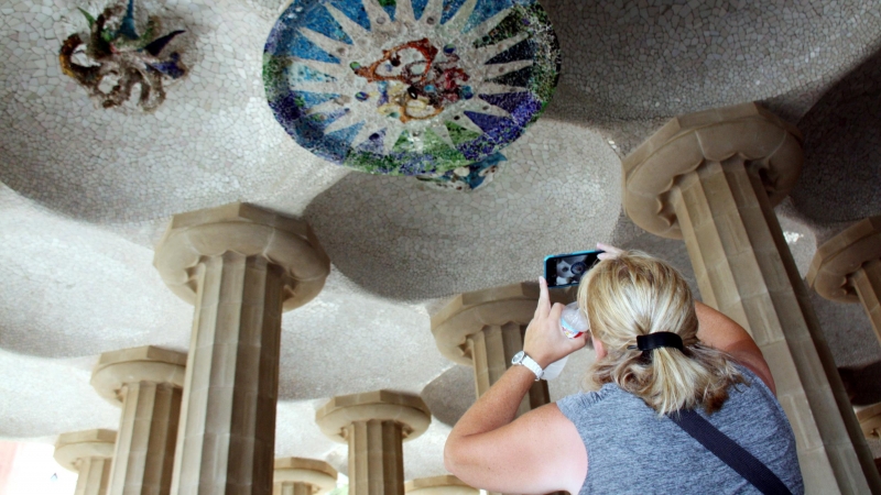 Una turista fotografia els medallons restaurats de la sala Hipòstila del Parc Güell.