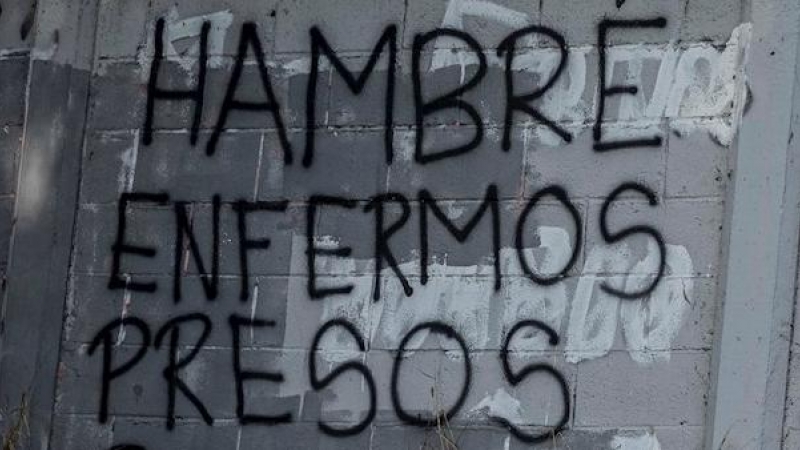 Una mujer camina frente a una pared con un graffiti pintado que dice 'Hambre, enfermos, presos, refugiados' el 8 de febrero de 2021, en Caracas (Venezuela).