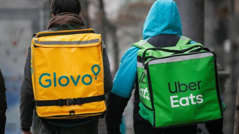 Un 'rider' de Glovo y otro de Uber Eats caminan por una calle principal .Reuters
