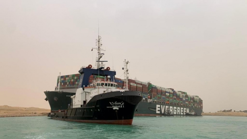Un barco vigila el buque portacontenedores que fue golpeado por un fuerte viento y encalló en el Canal de Suez, Egipto.