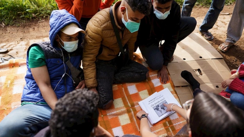 En la imagen, una voluntaria enseña algunas frases en español a un grupo de inmigrantes en el exterior del campamento.