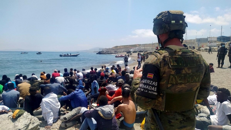 Un soldado del Ejército de Tierra observa a un grupo de migrantes que han logrado cruzar uno de los espigones fronterizos de Ceuta este martes en una avalancha de inmigrantes sin precedentes en España al registrarse la entrada en 24 horas de 5.000 persona